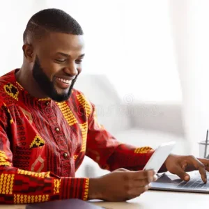 cheerful-black-man-traditional-african-clothes-using-smartphone-laptop-cheerful-black-man-traditional-african-clothes-389803045